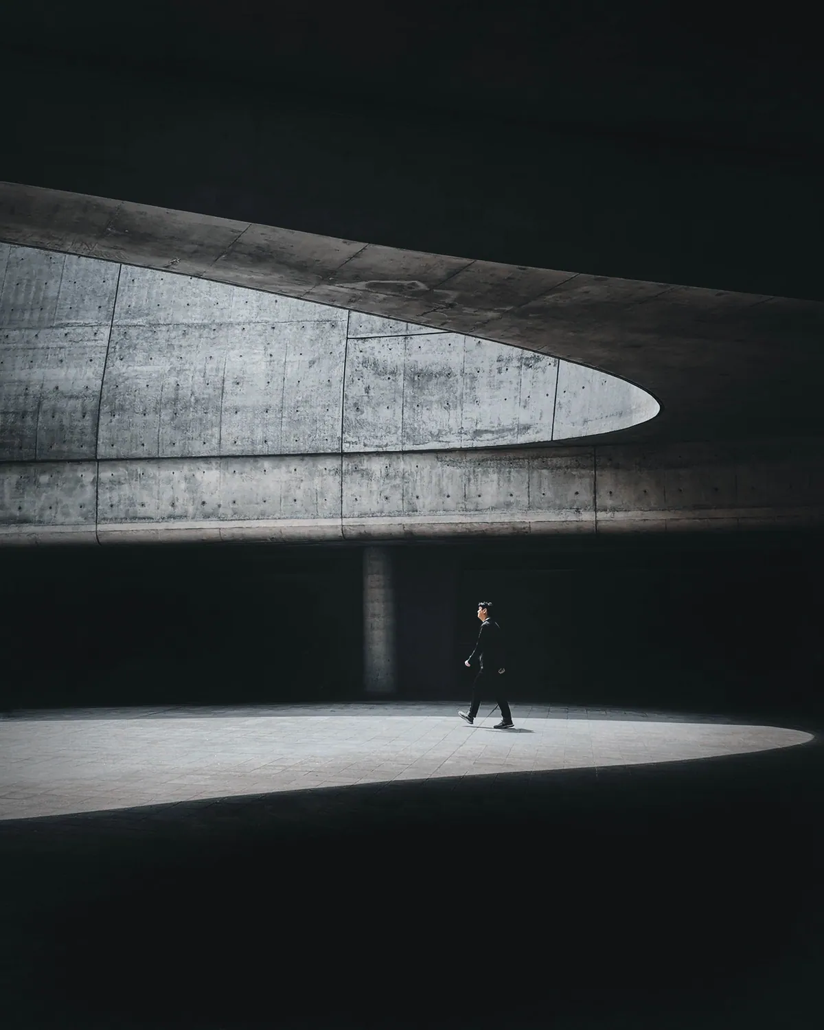 A person crosses a pool of light beneath curved concrete architecture in Seoul