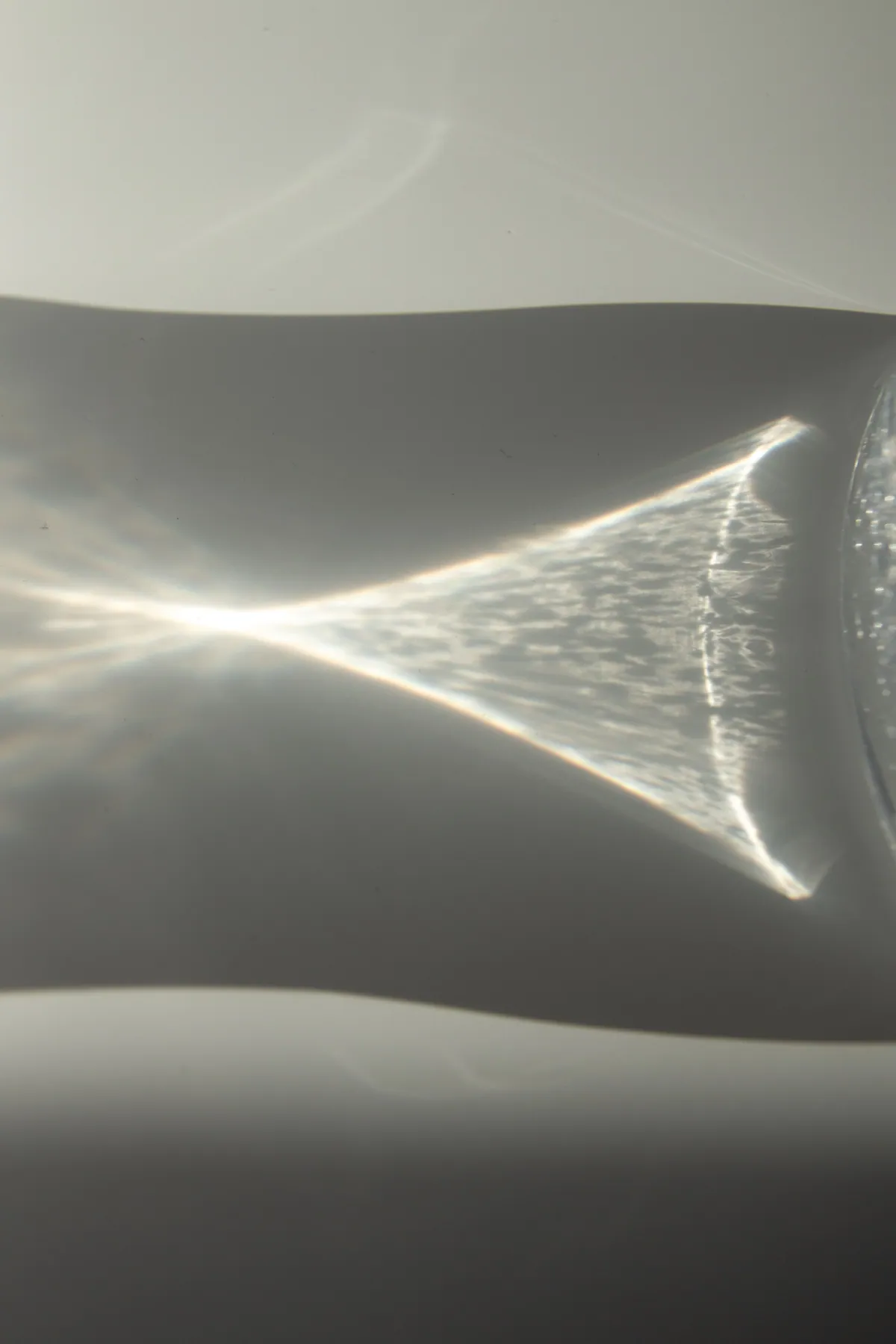 A glass vessel refracts a triangular beam of light onto a pale surface