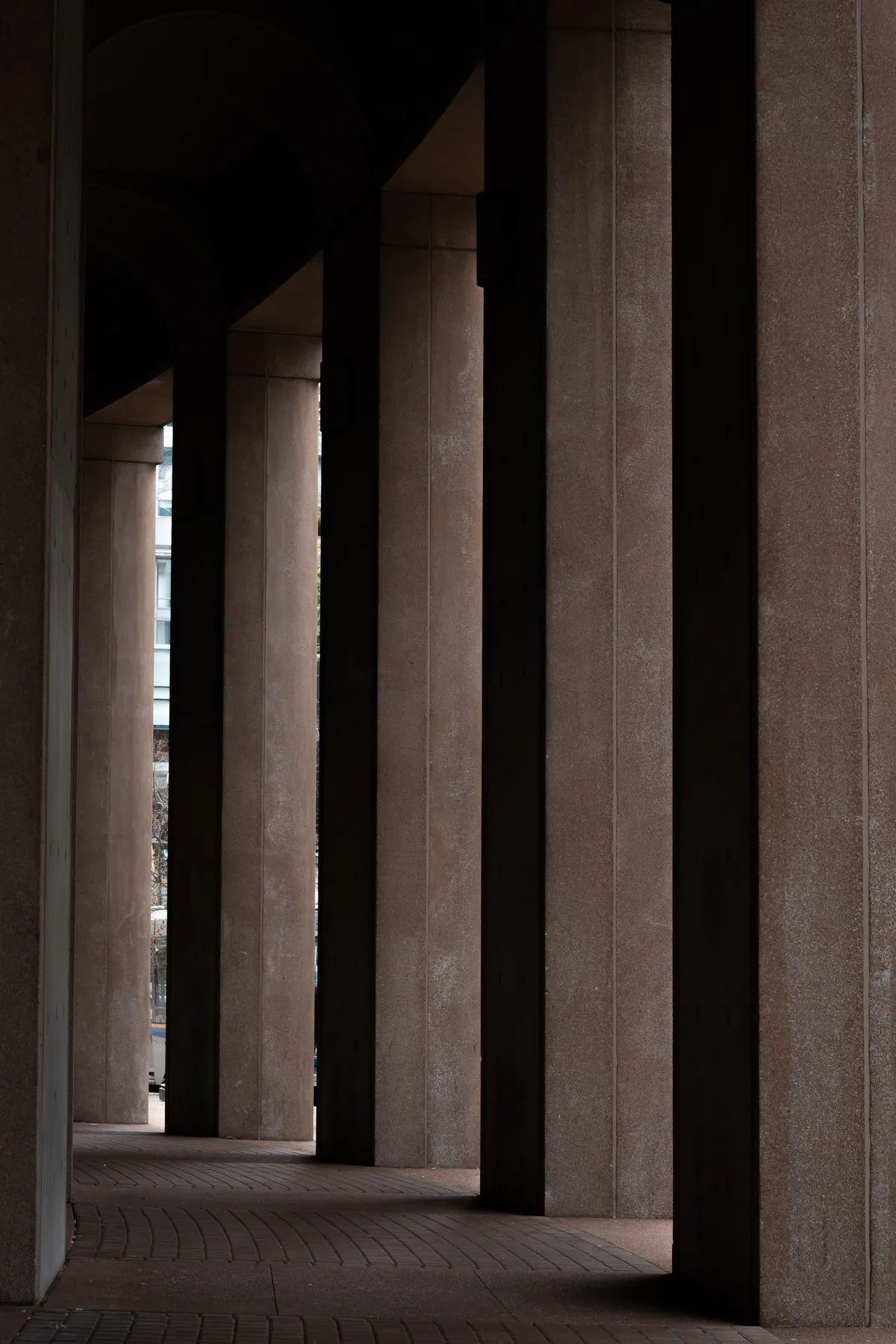 A sequence of concrete columns recedes towards a narrow opening of daylight